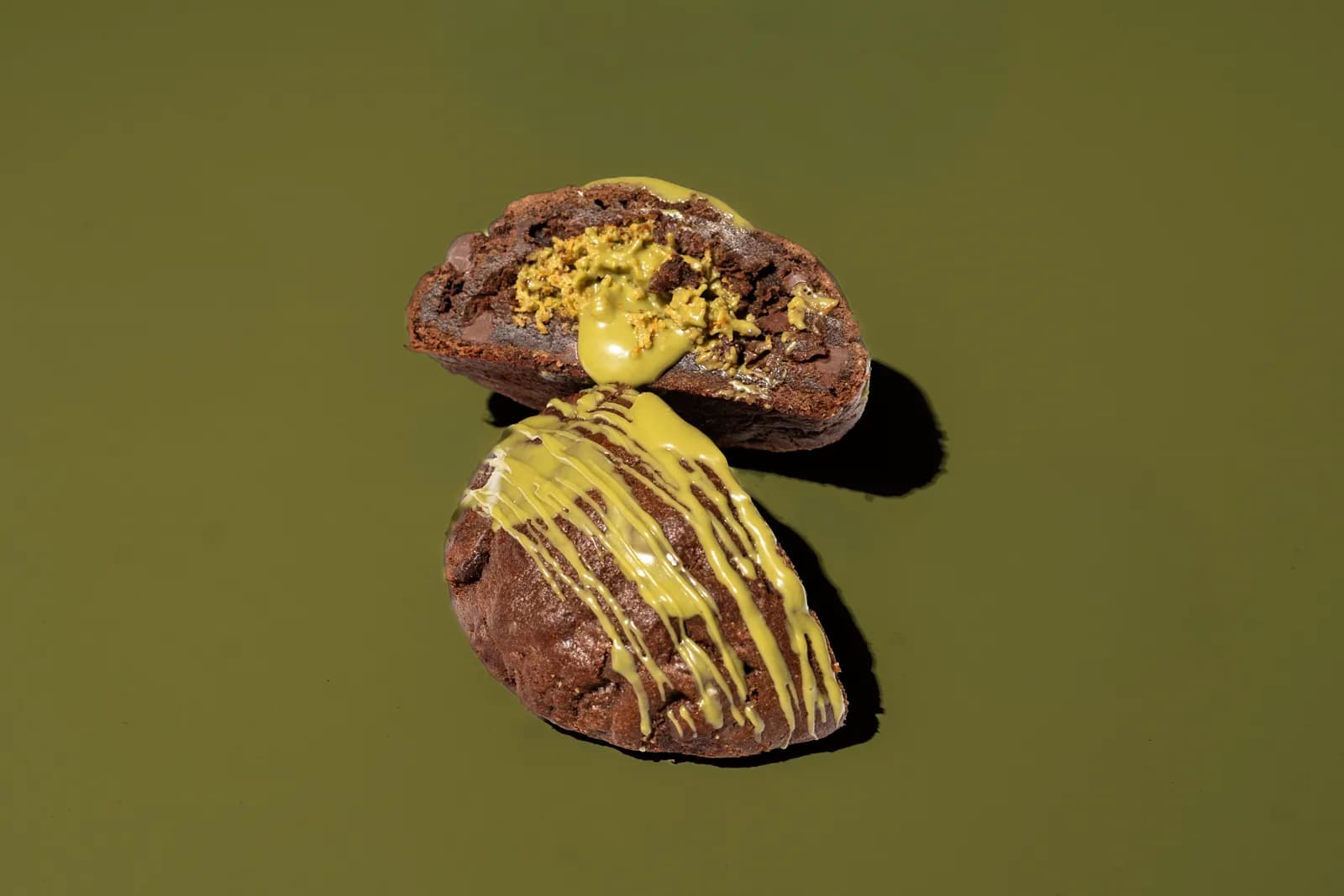 A pistachio cookie broken open on an olive green background.