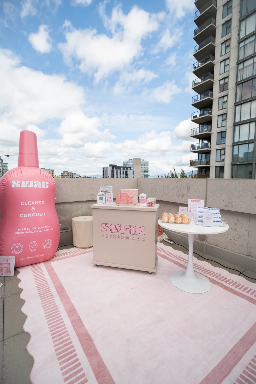An inflatable branded bottle standing beside the product table on a patterned rug, against the skyline.