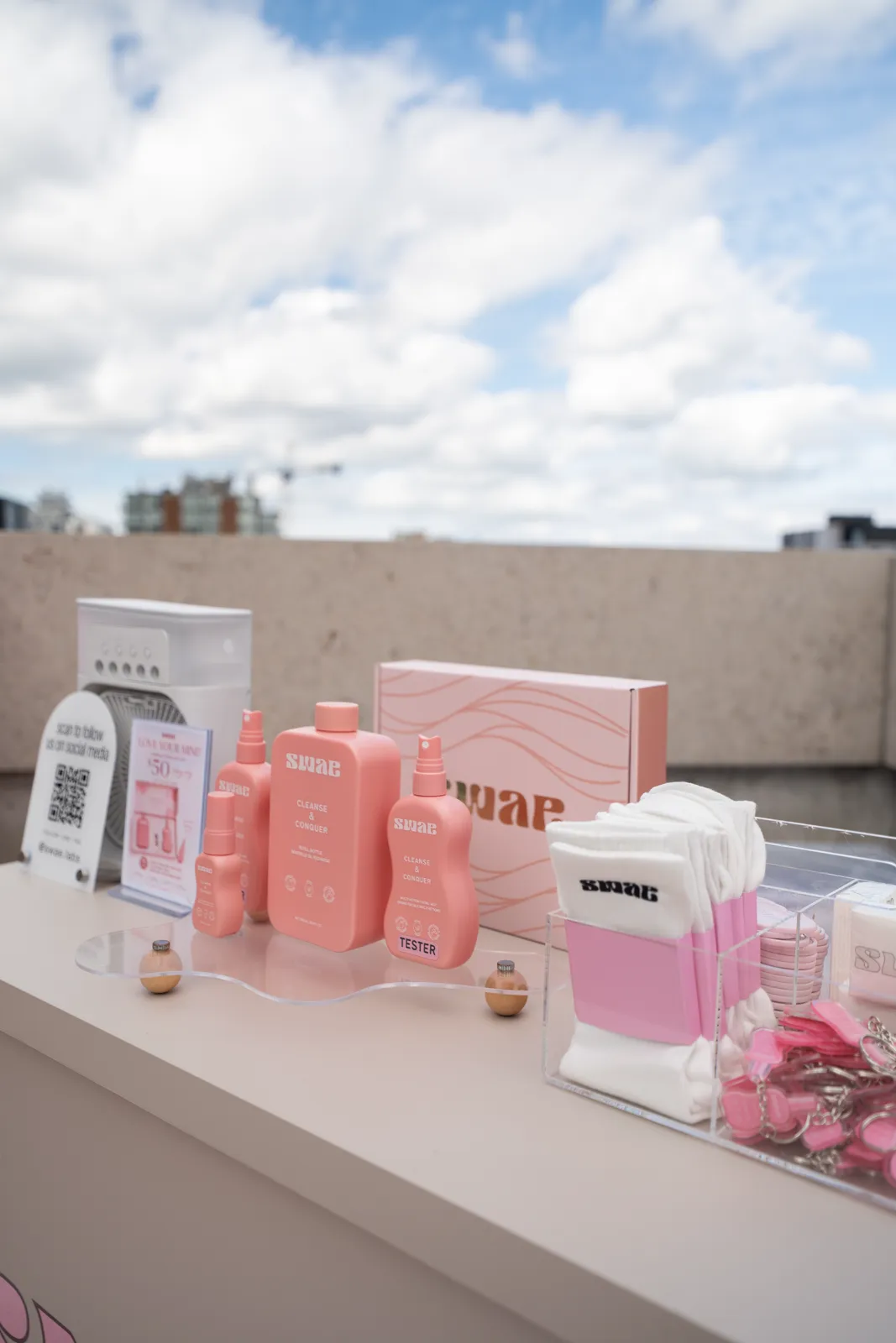 The product table in close-up: bottles, a tester, a boxed set and branded socks under an open sky.