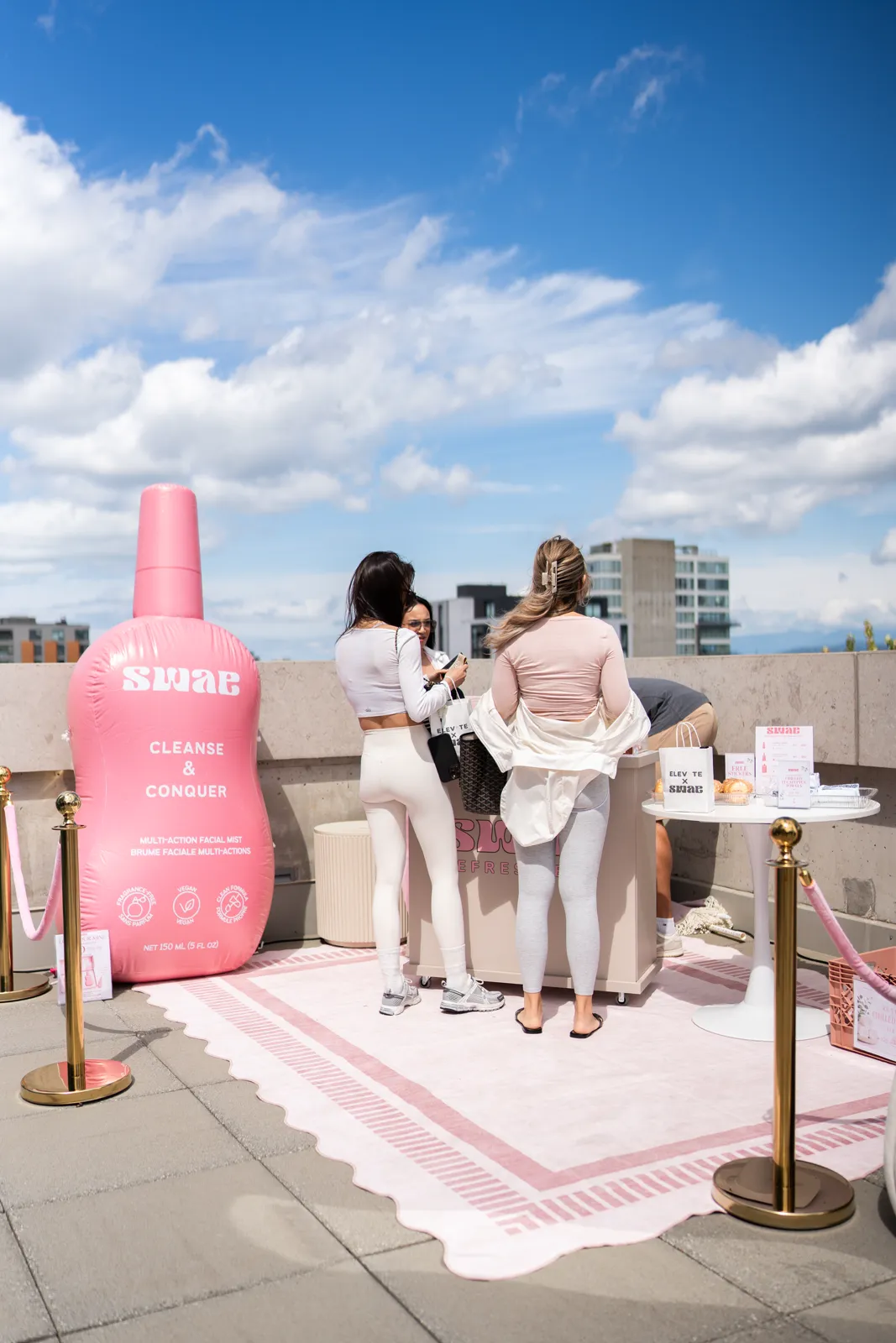 Attendees gathered at the product table beside the inflatable bottle, inside a roped-off set.