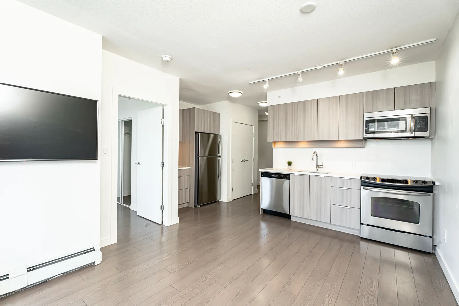 A vacant Surrey condo shot as an HDR interior set: an open kitchen under a track run, the living end from two angles, and a balcony outlook onto the towers.