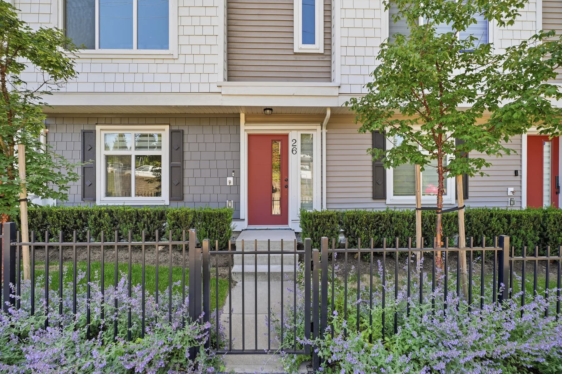 A townhouse unit with a red door and lavender planting at the front, an island kitchen under a pendant run, dining open to the living end, and a bright main bathroom.