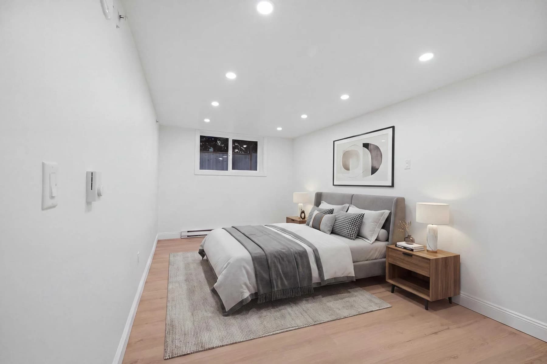 The same bedroom furnished digitally with a bed, side table, lamp, rug and framed art.